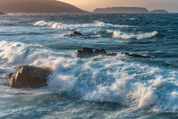 Удивительная сила волн, бьющихся о скалы во время заката. Большая океанская волна пробивает берег. Красота концепции природы. Красивый морской пейзаж. Обои, фон.