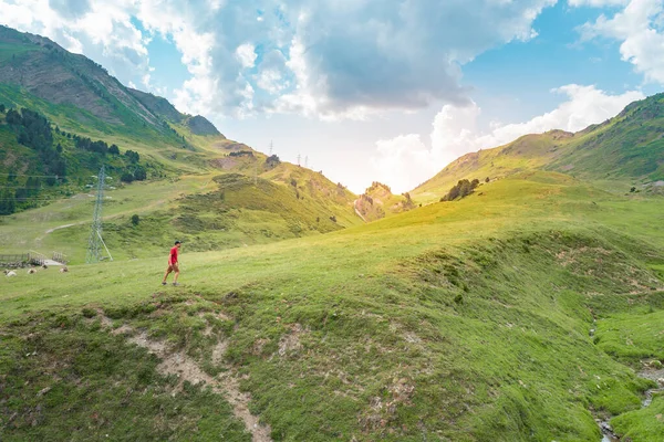 Amazing landscape with attractive man with red shirt standing on the top of a green mountain enjoying the view. Paradise grass mountain. Lifestyle relax and freedom. The beauty of nature concept.