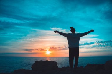 Uçurumun kenarında nefes alan güzel bir kadının silueti ve güzel renkli gökyüzü ile muhteşem bir denize bakıyor. Zevk, özgürlük ve rahatlama. Seyahat ve tatil kavramı. Sağlıklı zihin.