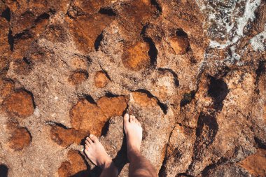 Çıplak ayaklı genç adamın bakış açısı deniz sahilindeki suda ay taşları üzerinde duruyor. Akdeniz yaz tatillerinde dinlenir.