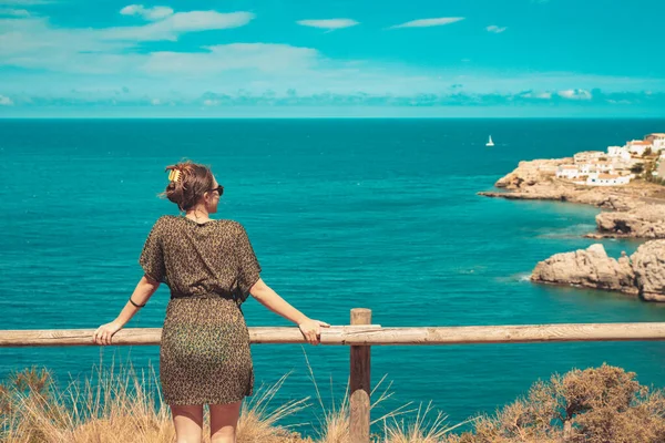 Beautiful woman standing and enjoy watching the sea view at balcony. Summer vibes. Adventure and travel female with leopard dress and sunglasses. Freedom, vacation and relax concept.