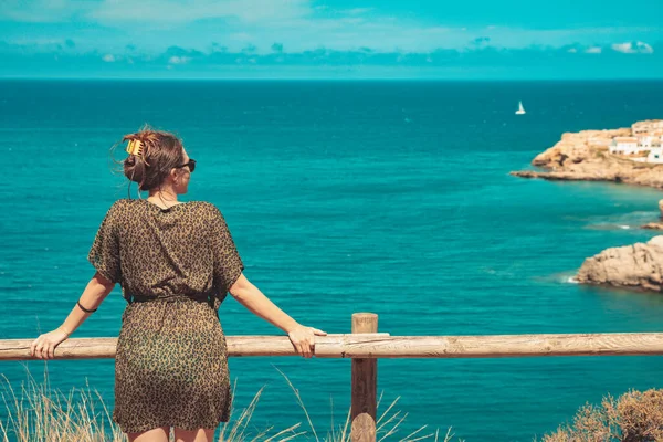 Beautiful woman standing and enjoy watching the sea view at balcony. Summer vibes. Adventure and travel female with leopard dress and sunglasses. Freedom, vacation and relax concept.