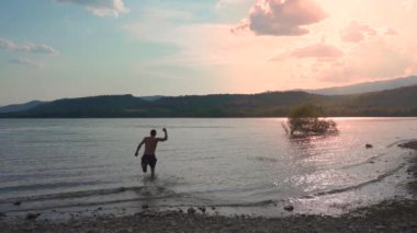 Çekici bir adam kristal berrak suya balıklama atlıyor ve yavaş çekimde nehirde yüzüyor. Yaz atmosferi ve tatil konsepti. 