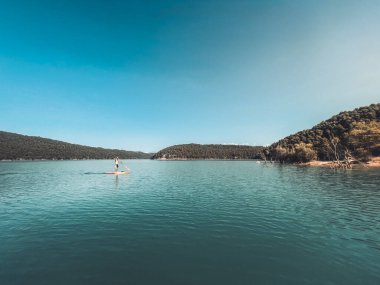 Çekici ve güçlü bir adam gölde şeffaf suların tadını çıkarıyor. Tropik seyahat, seyahat tutkusu ve su aktivitesi konsepti. Paddle Surf su sporları. Yaz tatilleri.