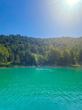 Çekici ve güçlü bir adam gölde şeffaf suların tadını çıkarıyor. Tropik seyahat, seyahat tutkusu ve su aktivitesi konsepti. Paddle Surf su sporları. Yaz tatilleri.