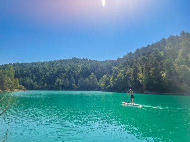 Yemek masasında güzel ve güçlü bir kadın gölde şeffaf suların tadını çıkarıyor. Tropik seyahat, seyahat tutkusu ve su aktivitesi konsepti. Paddle Surf su sporları. Yaz tatilleri.