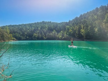 Yemek masasında güzel ve güçlü bir kadın gölde şeffaf suların tadını çıkarıyor. Tropik seyahat, seyahat tutkusu ve su aktivitesi konsepti. Paddle Surf su sporları. Yaz tatilleri.