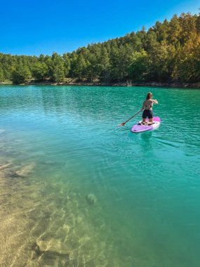 Yemek masasında güzel ve güçlü bir kadın gölde şeffaf suların tadını çıkarıyor. Tropik seyahat, seyahat tutkusu ve su aktivitesi konsepti. Paddle Surf su sporları. Yaz tatilleri.