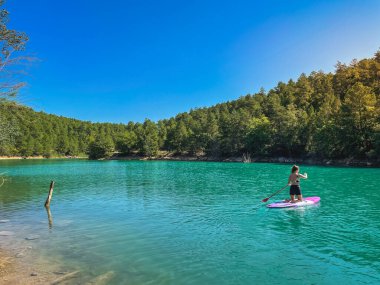 Yemek masasında güzel ve güçlü bir kadın gölde şeffaf suların tadını çıkarıyor. Tropik seyahat, seyahat tutkusu ve su aktivitesi konsepti. Paddle Surf su sporları. Yaz tatilleri.