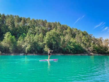Yemek masasında güzel ve güçlü bir kadın gölde şeffaf suların tadını çıkarıyor. Tropik seyahat, seyahat tutkusu ve su aktivitesi konsepti. Paddle Surf su sporları. Yaz tatilleri.