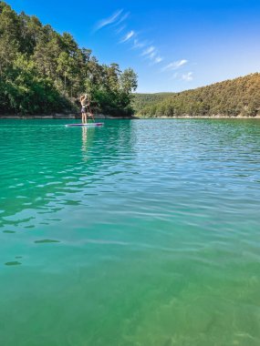 Yemek masasında güzel ve güçlü bir kadın gölde şeffaf suların tadını çıkarıyor. Tropik seyahat, seyahat tutkusu ve su aktivitesi konsepti. Paddle Surf su sporları. Yaz tatilleri.