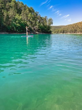 Yemek masasında güzel ve güçlü bir kadın gölde şeffaf suların tadını çıkarıyor. Tropik seyahat, seyahat tutkusu ve su aktivitesi konsepti. Paddle Surf su sporları. Yaz tatilleri.