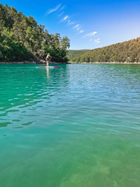 Yemek masasında güzel ve güçlü bir kadın gölde şeffaf suların tadını çıkarıyor. Tropik seyahat, seyahat tutkusu ve su aktivitesi konsepti. Paddle Surf su sporları. Yaz tatilleri.