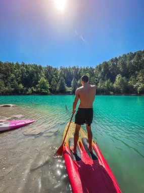 Çekici ve güçlü bir adam gölde şeffaf suların tadını çıkarıyor. Tropik seyahat, seyahat tutkusu ve su aktivitesi konsepti. Paddle Surf su sporları. Yaz tatilleri.