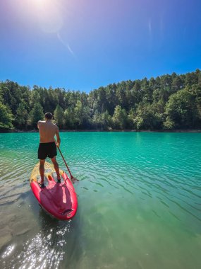 Çekici ve güçlü bir adam gölde şeffaf suların tadını çıkarıyor. Tropik seyahat, seyahat tutkusu ve su aktivitesi konsepti. Paddle Surf su sporları. Yaz tatilleri.