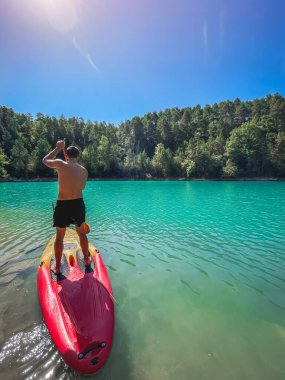 Çekici ve güçlü bir adam gölde şeffaf suların tadını çıkarıyor. Tropik seyahat, seyahat tutkusu ve su aktivitesi konsepti. Paddle Surf su sporları. Yaz tatilleri.
