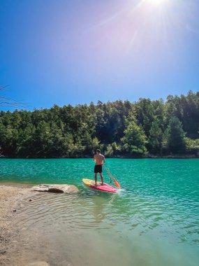 Çekici ve güçlü bir adam gölde şeffaf suların tadını çıkarıyor. Tropik seyahat, seyahat tutkusu ve su aktivitesi konsepti. Paddle Surf su sporları. Yaz tatilleri.