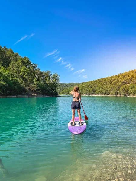 Yemek masasında güzel ve güçlü bir kadın gölde şeffaf suların tadını çıkarıyor. Tropik seyahat, seyahat tutkusu ve su aktivitesi konsepti. Paddle Surf su sporları. Yaz tatilleri.