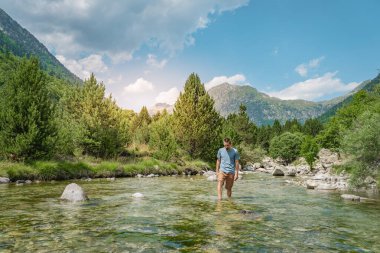 Genç adam gün batımında güzel bir manzarada nehrin içinde yürüyor. Doğal ve vahşi yaşam tarzı rahatlama, kopukluk ve özgürlük kavramı. Seyahat ve tatil kavramı.