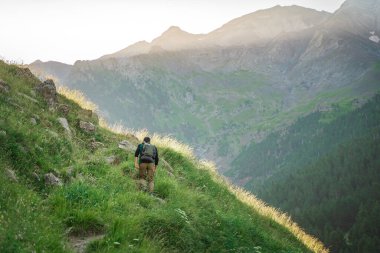 Genç adam yeşil bir dağın tepesinde gün batımında muhteşem manzara manzarasının tadını çıkarıyor. Cennet çim dağı. Yaşam tarzı rahatlama ve özgürlük. Doğa kavramının güzelliği.