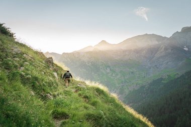 Genç adam yeşil bir dağın tepesinde gün batımında muhteşem manzara manzarasının tadını çıkarıyor. Cennet çim dağı. Yaşam tarzı rahatlama ve özgürlük. Doğa kavramının güzelliği.