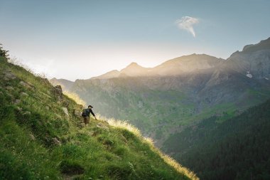 Genç adam yeşil bir dağın tepesinde gün batımında muhteşem manzara manzarasının tadını çıkarıyor. Cennet çim dağı. Yaşam tarzı rahatlama ve özgürlük. Doğa kavramının güzelliği.