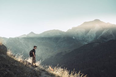 Genç adam yeşil bir dağın tepesinde gün batımında muhteşem manzara manzarasının tadını çıkarıyor. Cennet çim dağı. Yaşam tarzı rahatlama ve özgürlük. Doğa kavramının güzelliği.