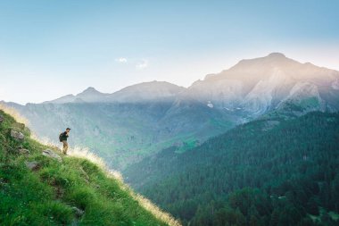 Genç adam yeşil bir dağın tepesinde gün batımında muhteşem manzara manzarasının tadını çıkarıyor. Cennet çim dağı. Yaşam tarzı rahatlama ve özgürlük. Doğa kavramının güzelliği.