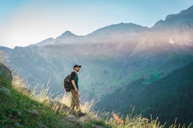Genç adam yeşil bir dağın tepesinde gün batımında muhteşem manzara manzarasının tadını çıkarıyor. Cennet çim dağı. Yaşam tarzı rahatlama ve özgürlük. Doğa kavramının güzelliği.