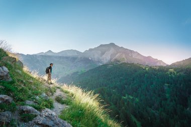 Genç adam yeşil bir dağın tepesinde gün batımında muhteşem manzara manzarasının tadını çıkarıyor. Cennet çim dağı. Yaşam tarzı rahatlama ve özgürlük. Doğa kavramının güzelliği.