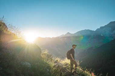 Genç adam yeşil bir dağın tepesinde gün batımında muhteşem manzara manzarasının tadını çıkarıyor. Cennet çim dağı. Yaşam tarzı rahatlama ve özgürlük. Doğa kavramının güzelliği.