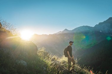 Genç adam yeşil bir dağın tepesinde gün batımında muhteşem manzara manzarasının tadını çıkarıyor. Cennet çim dağı. Yaşam tarzı rahatlama ve özgürlük. Doğa kavramının güzelliği.