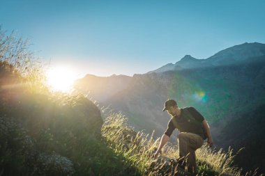 Genç adam yeşil bir dağın tepesinde gün batımında muhteşem manzara manzarasının tadını çıkarıyor. Cennet çim dağı. Yaşam tarzı rahatlama ve özgürlük. Doğa kavramının güzelliği.