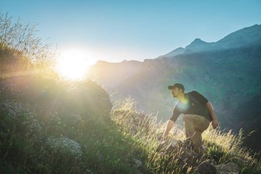 Genç adam yeşil bir dağın tepesinde gün batımında muhteşem manzara manzarasının tadını çıkarıyor. Cennet çim dağı. Yaşam tarzı rahatlama ve özgürlük. Doğa kavramının güzelliği.