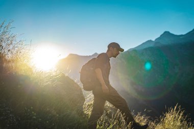 Genç adam yeşil bir dağın tepesinde gün batımında muhteşem manzara manzarasının tadını çıkarıyor. Cennet çim dağı. Yaşam tarzı rahatlama ve özgürlük. Doğa kavramının güzelliği.