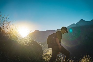 Genç adam yeşil bir dağın tepesinde gün batımında muhteşem manzara manzarasının tadını çıkarıyor. Cennet çim dağı. Yaşam tarzı rahatlama ve özgürlük. Doğa kavramının güzelliği.