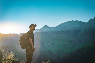Genç adam yeşil bir dağın tepesinde gün batımında muhteşem manzara manzarasının tadını çıkarıyor. Cennet çim dağı. Yaşam tarzı rahatlama ve özgürlük. Doğa kavramının güzelliği.