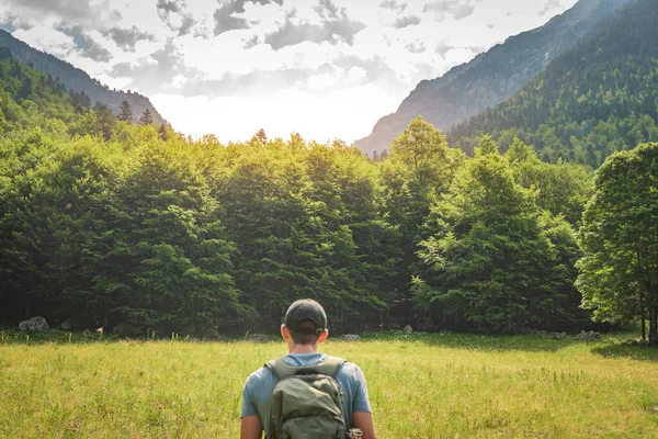 Shot from the back of a young man trekking on the top of a green mountain enjoying the amazing landscape views during sunset. Paradise grass mountain. Lifestyle relax and freedom.