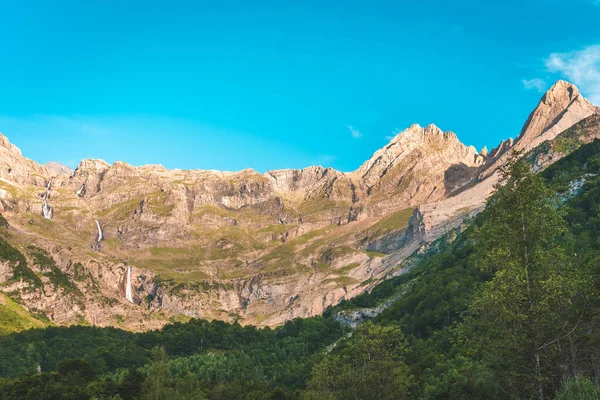 Beautiful mountains landscape with waterfalls and rivers during sunset. A scenic view of a colorful sky above the mountains. Orange and blue clouds. Adventure travel concept. Wallpaper background nature print.