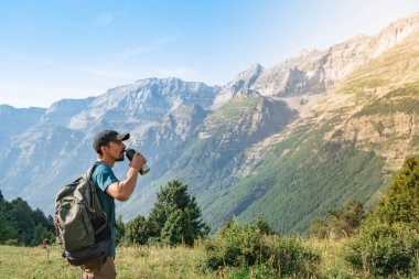 Gün batımında muhteşem manzara manzarası olan yeşil bir dağın tepesinde tatlı su içmek. Cennet çim dağı. Spor ve sağlıklı aktiviteler. Su iç konsepti.