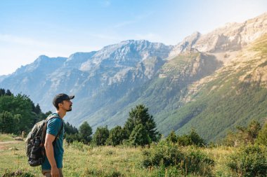 Genç adam yeşil bir dağın tepesinde gün batımında muhteşem manzara manzarasının tadını çıkarıyor. Cennet çim dağı. Yaşam tarzı rahatlama ve özgürlük. Doğa kavramının güzelliği.
