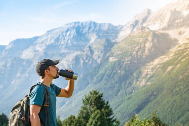 Gün batımında muhteşem manzara manzarası olan yeşil bir dağın tepesinde tatlı su içmek. Cennet çim dağı. Spor ve sağlıklı aktiviteler. Su iç konsepti.