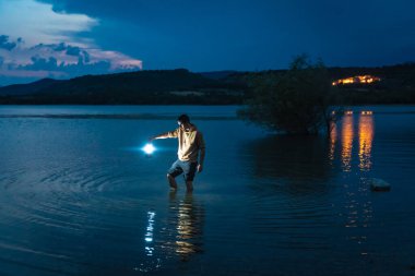 Gece vakti elinde fenerle göldeki suyun içindeki genç adam. Güneş ışığı, çocuğun güzel manzaraya bakışını gösterir. Karanlıkta tek başına. Antika bir fener gece yolu aydınlatıyor. Umut kavramı.