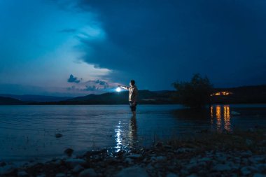 Gece vakti elinde fenerle göldeki suyun içindeki genç adam. Güneş ışığı, çocuğun güzel manzaraya bakışını gösterir. Karanlıkta tek başına. Antika bir fener gece yolu aydınlatıyor. Umut kavramı.