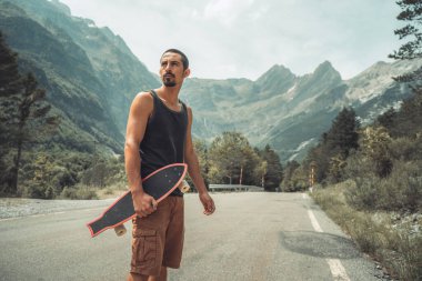 Genç hippi elinde havalı bir uzun tahta tutuyor. Güzel bir seyahat konsepti. Milenyum macera yolculuğu. Kaykay kaykay gezisi. Vahşi doğada spor.