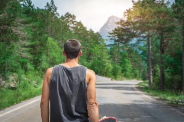 Genç hippi elinde havalı bir uzun tahta tutuyor. Güzel bir seyahat konsepti. Milenyum macera yolculuğu. Kaykay kaykay gezisi. Vahşi doğada spor.