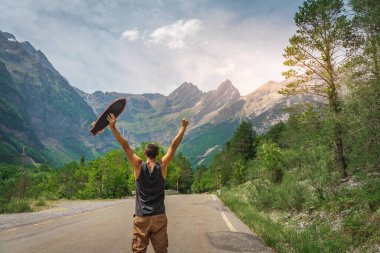 Genç hippi elinde havalı bir uzun tahta tutuyor. Güzel bir seyahat konsepti. Milenyum macera yolculuğu. Kaykay kaykay gezisi. Vahşi doğada spor.
