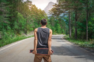 Genç hippi elinde havalı bir uzun tahta tutuyor. Güzel bir seyahat konsepti. Milenyum macera yolculuğu. Kaykay kaykay gezisi. Vahşi doğada spor.