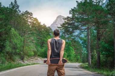 Genç hippi elinde havalı bir uzun tahta tutuyor. Güzel bir seyahat konsepti. Milenyum macera yolculuğu. Kaykay kaykay gezisi. Vahşi doğada spor.