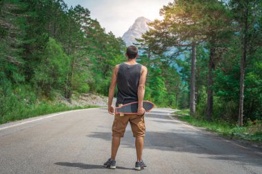 Genç hippi elinde havalı bir uzun tahta tutuyor. Güzel bir seyahat konsepti. Milenyum macera yolculuğu. Kaykay kaykay gezisi. Vahşi doğada spor.